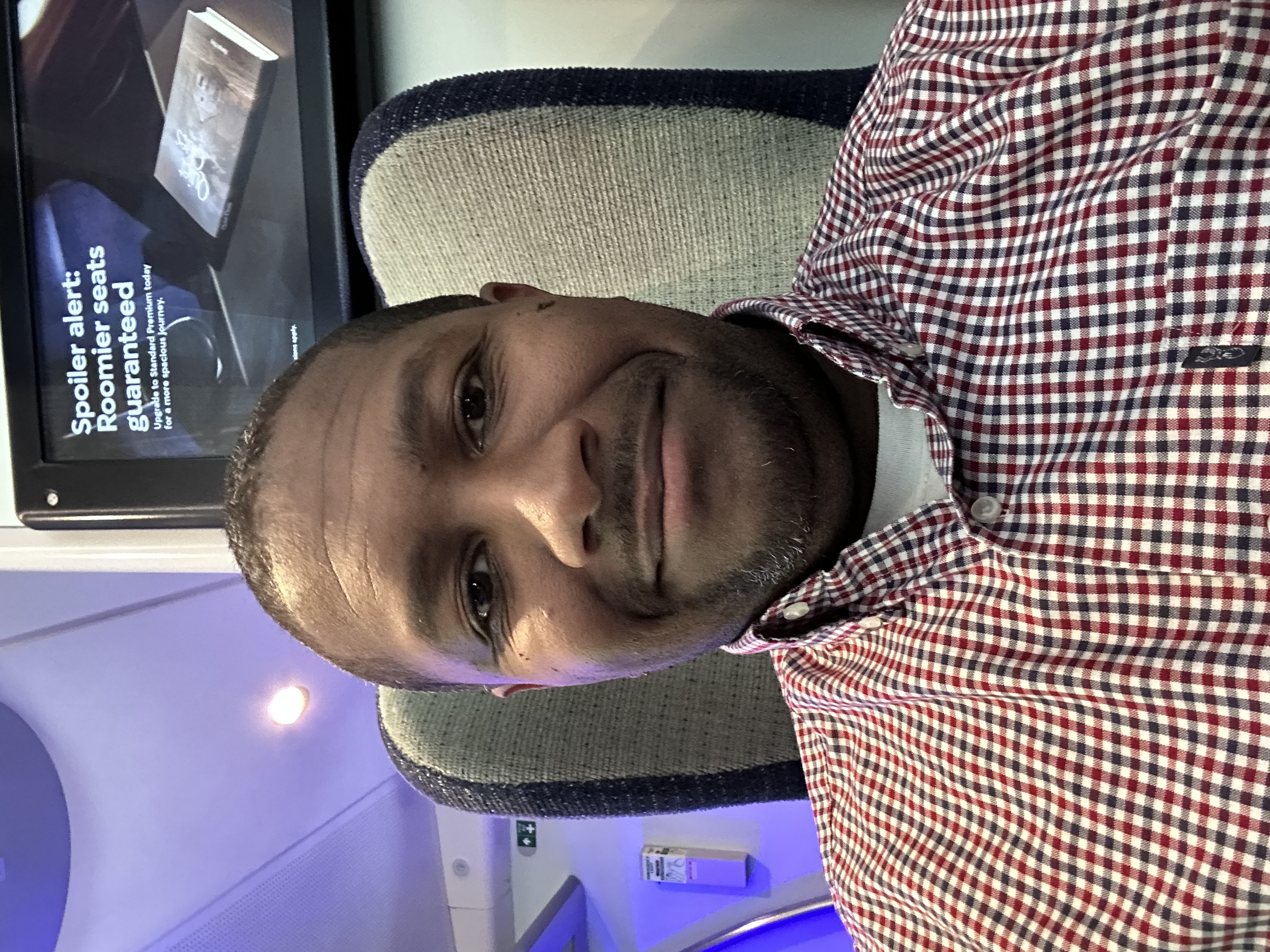 I’m smiling in a selfie wearing a blue and red checkered shirt. 