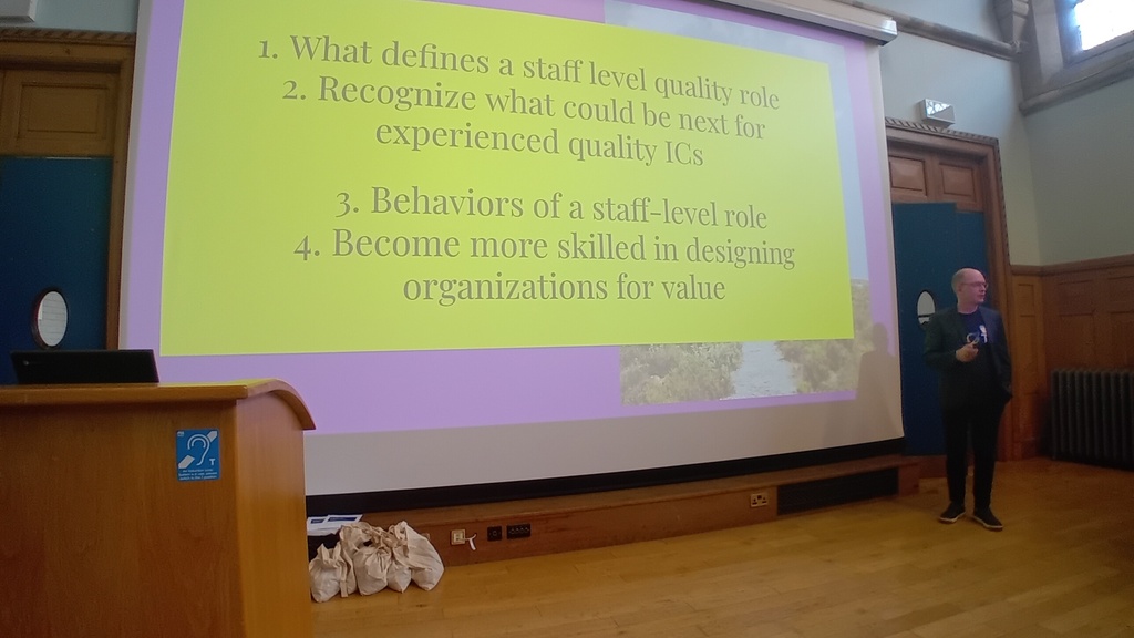 Photo of a man presenting in front of a screen, the slide has a yellow background. image