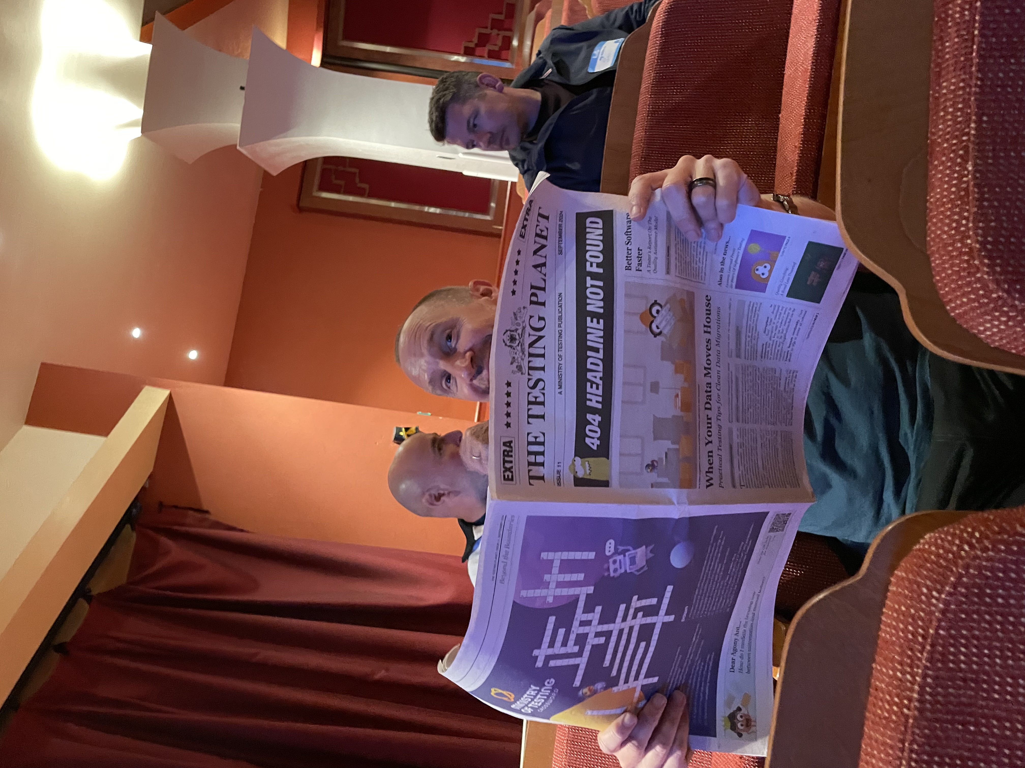 A photo of Simon Rigler sitting in the audience at TestBash Brighton holding up the newspaper "pretending" to read. 😃