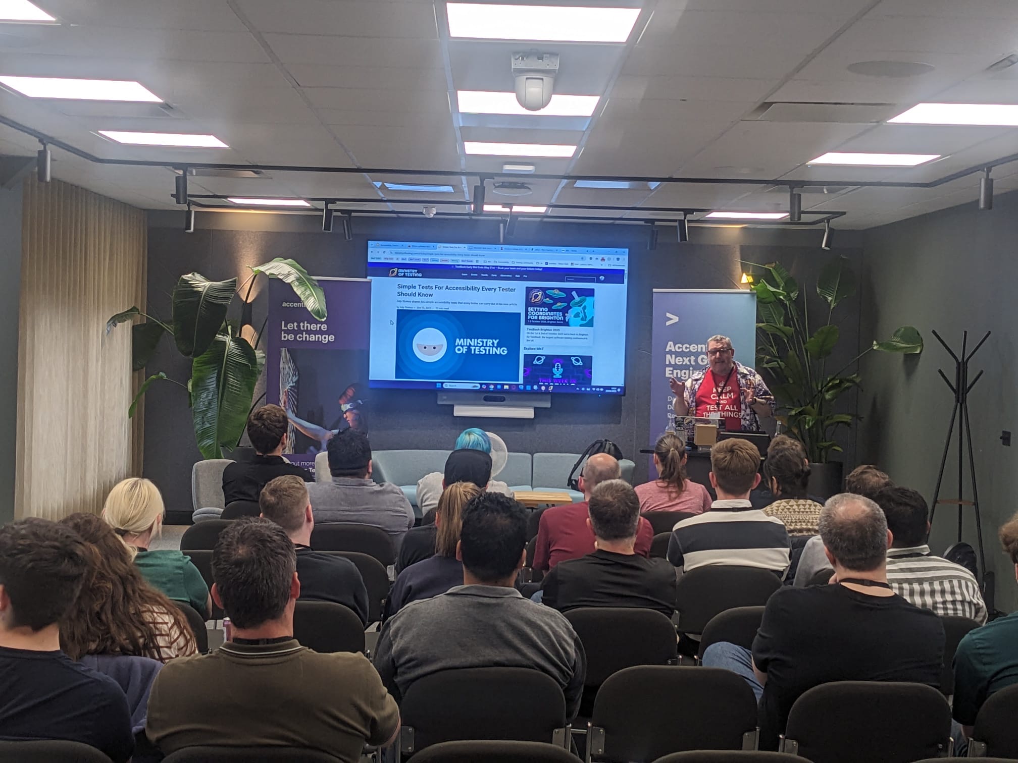 Ady Stokes presenting accessibility tests to an engaged MoT Leeds audience. Ady is wearing a red T-shirt and Hawaiian shirt with an accessibility is fundamental logo. 