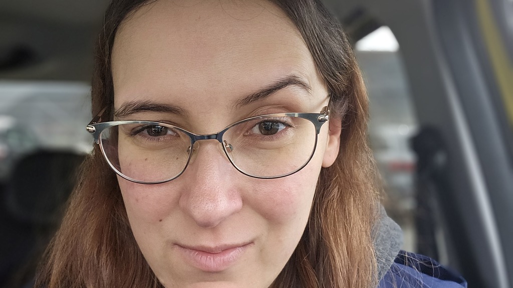 Picture of Demi (woman with long brown hear, brown eyes, glasses, wearing a blue coat) smiling and having one eyebrow... image