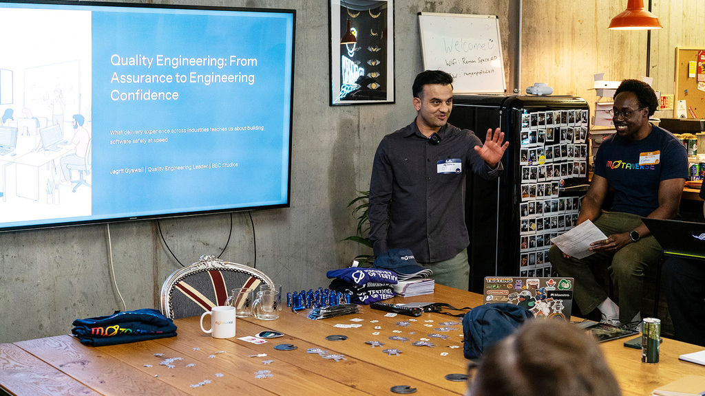 A photo of Jagrit Gyawali delivering his talk at MoT London. Jagrit is talking next to a display showing his presenta... image