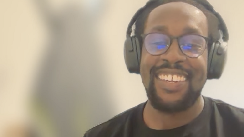 A man on a video call. There's a blurred ironing board in the background that looks a bit like the MoTaverse Bug char... image