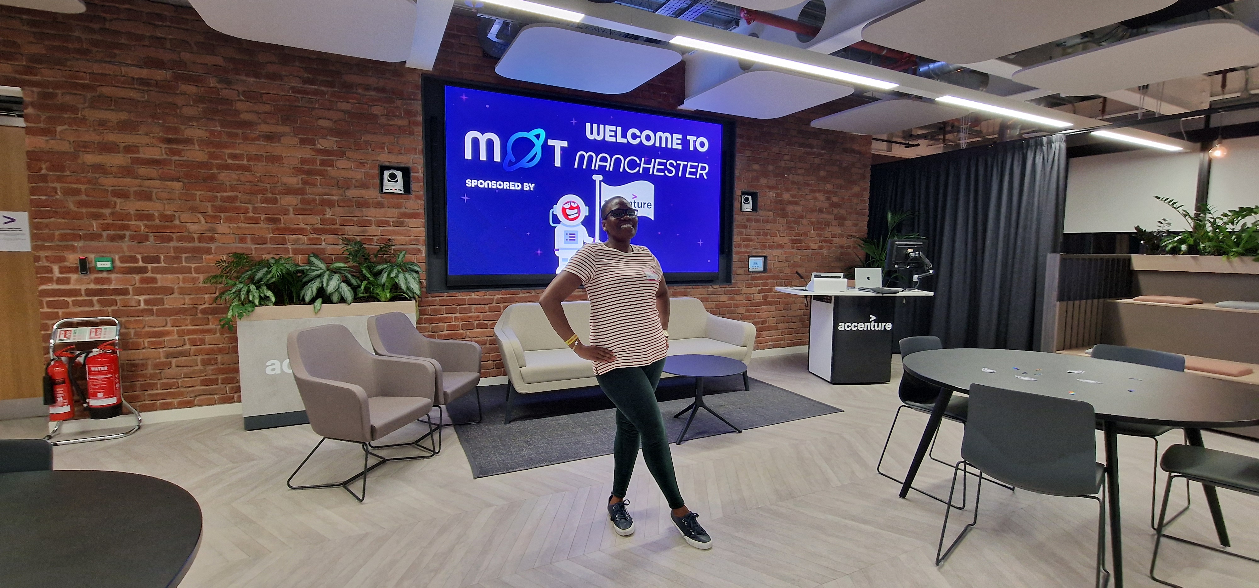 A person stands confidently with their hands on their hips in the center of a modern office lounge. They are wearing ... image