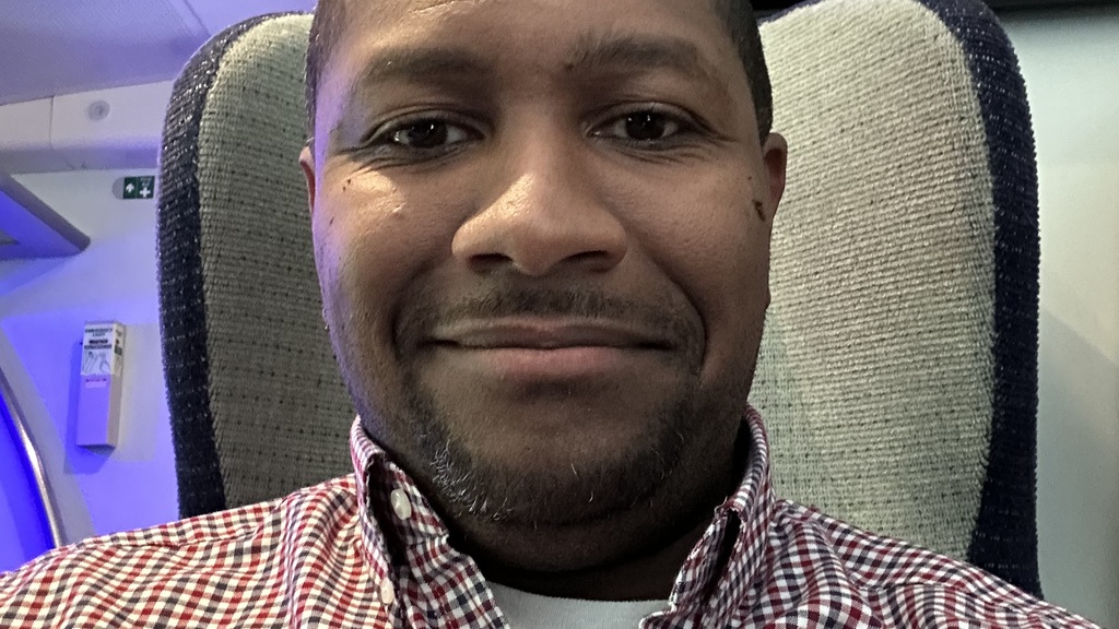 I’m smiling in a selfie wearing a blue and red checkered shirt. 