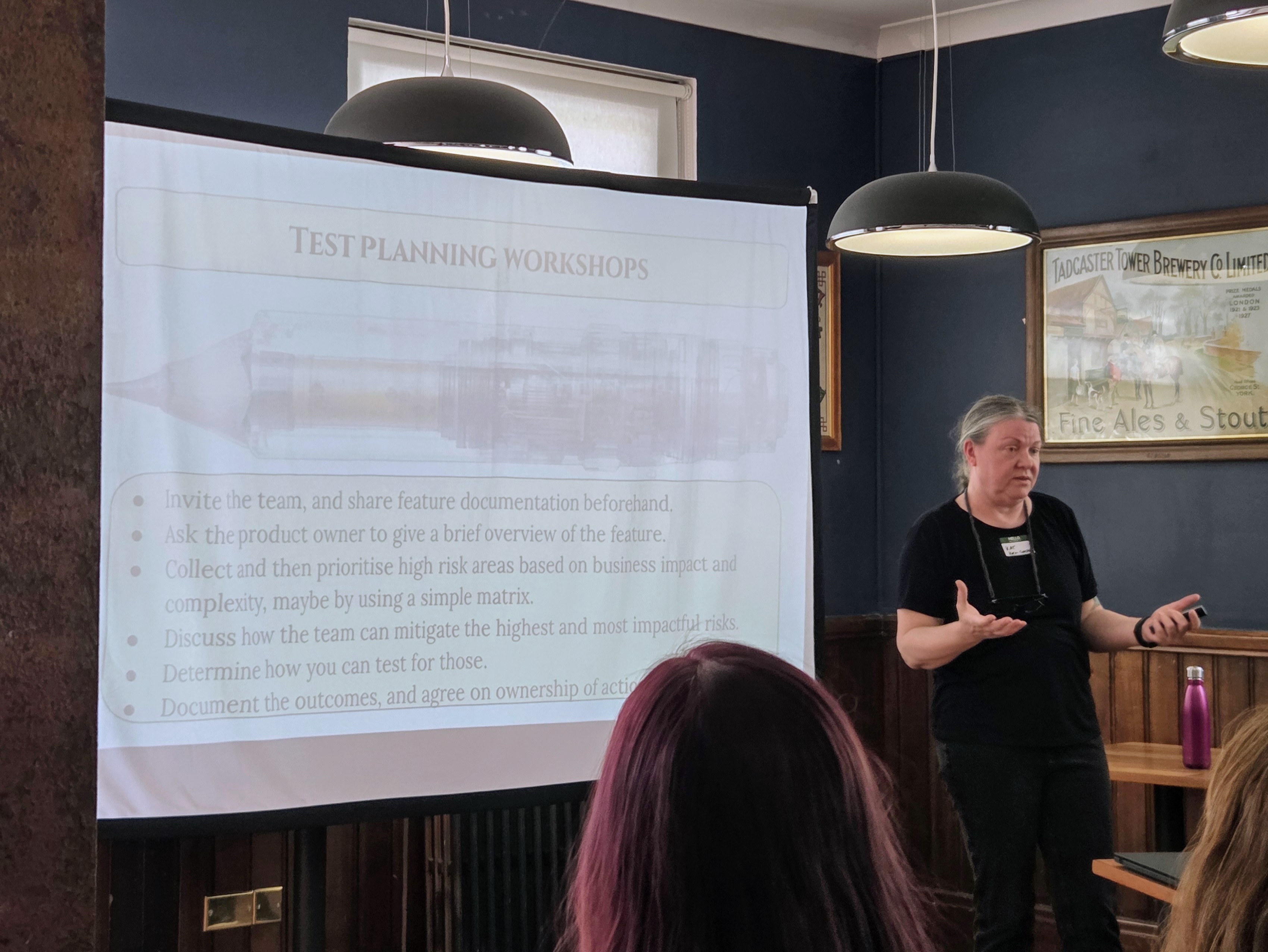 Kat Obring presenting at Leeds Testing Atelier, standing beside a projected slide titled “Test Planning Workshops,” which outlines steps for running collaborative test planning sessions.