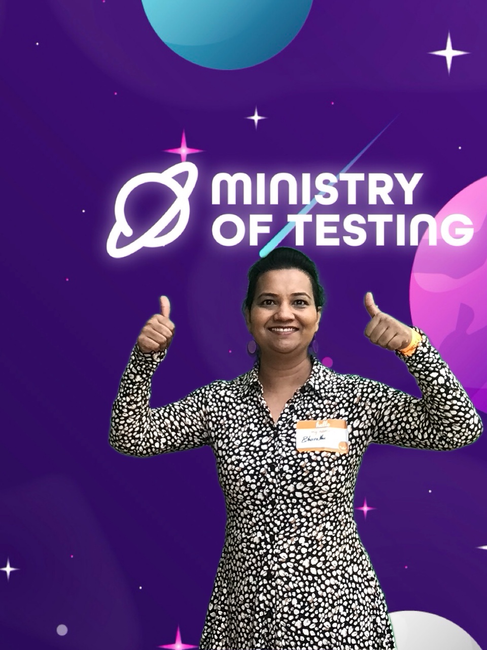Here we have a super strong solo pic. We are immediately greeted with a big smile and 2 thumbs up. This TestBash attendee wears a black and white patterned dress and wears their hair up with some lovely dangly earrings. They do have a name tag on but we can't quite make it out. 

Background: The green screen backdrop depicts a simple illustrated outer space scene. The main colour is purple, with cute stars and planets in shades of pink, blue, and white. About a third of the way down the screen, a logo appears. It reads "Ministry of Testing" in bold white text with a blue shooting star behind it. Next to the text, in the same bold white style, is a line drawing of the planet Saturn.