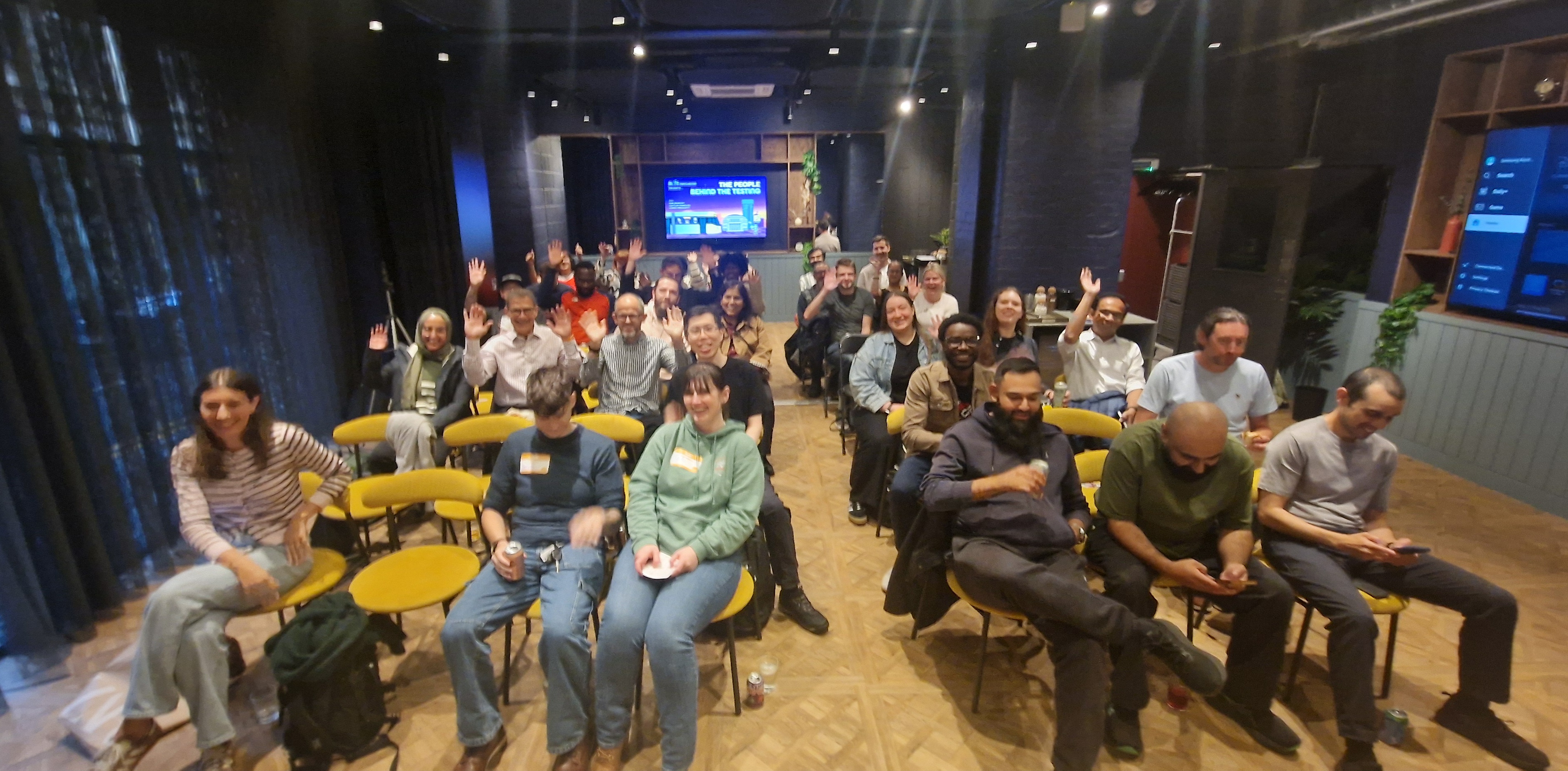 A diverse group of audience members seated in rows of yellow and black chairs inside a modern presentation room, with... image