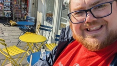 Ben Dowen, a white man with long ginger hair, wearing a red software testing clinic t-shirt. Holding a tray of chips, outside "the famous fish &amp; chips" chip shop in Brighton image