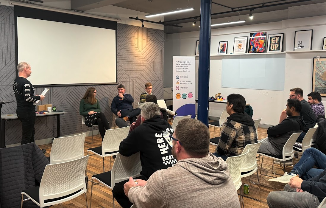 Meeting room at Hippo Digital. The panel is at the front with Colin, Emily, Scott and Adam. The view is from the back corner of the room with the audience listening closely. 