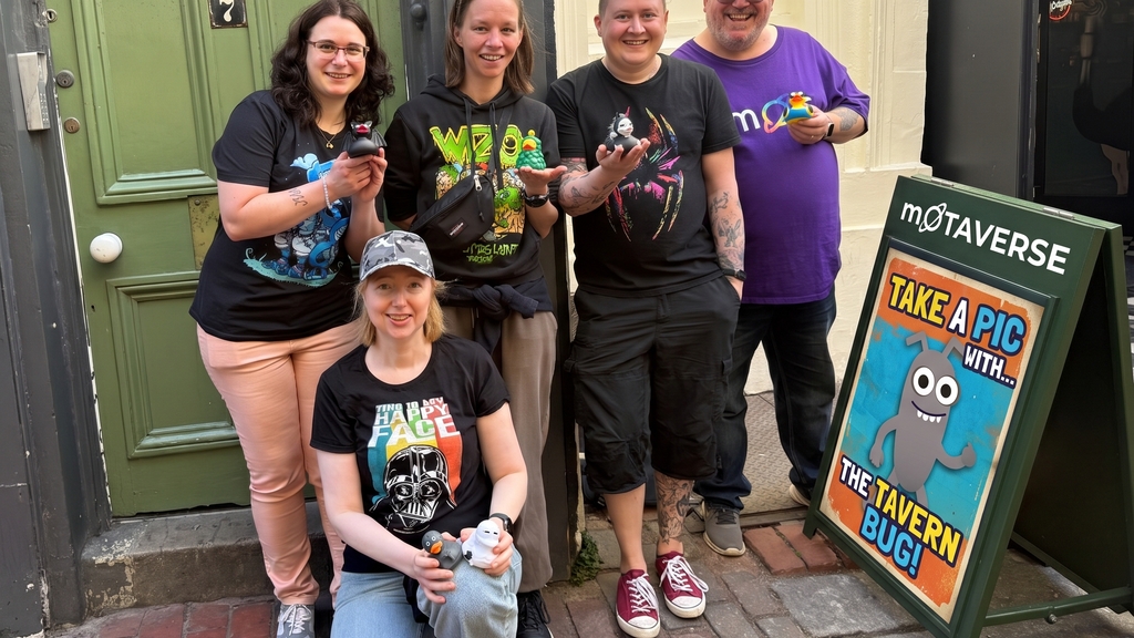 Displays a group of five smiling people posing outdoors on a brick street. Four are standing and one is kneeling, and... image