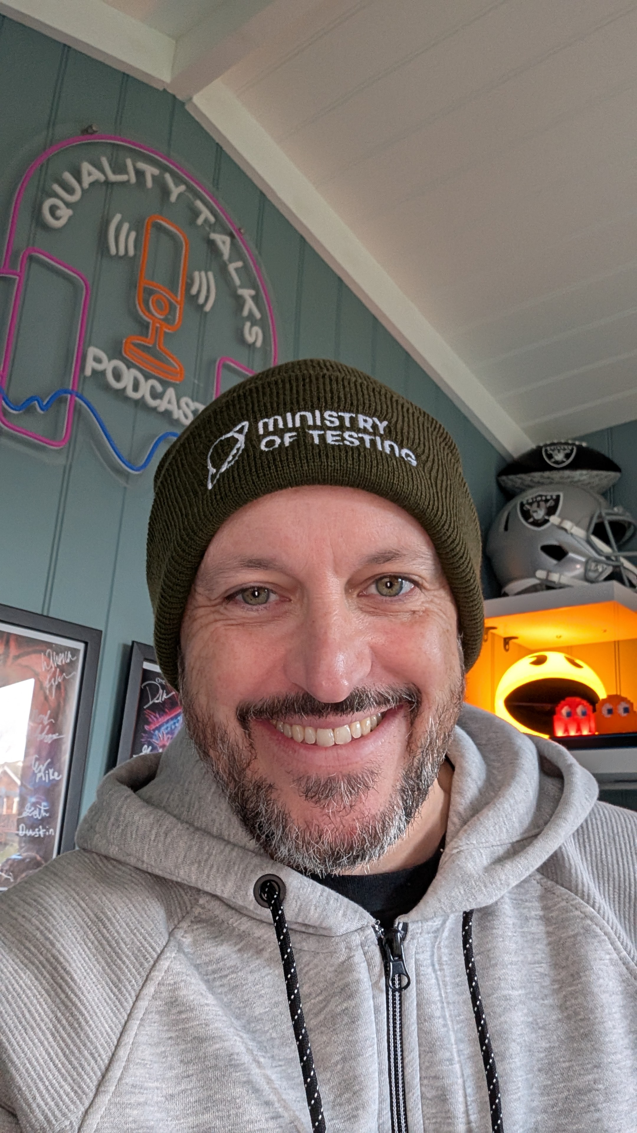 White male in a grey hoodie sitting at a desk wearing an olive green Ministry of Testing beanie in his head