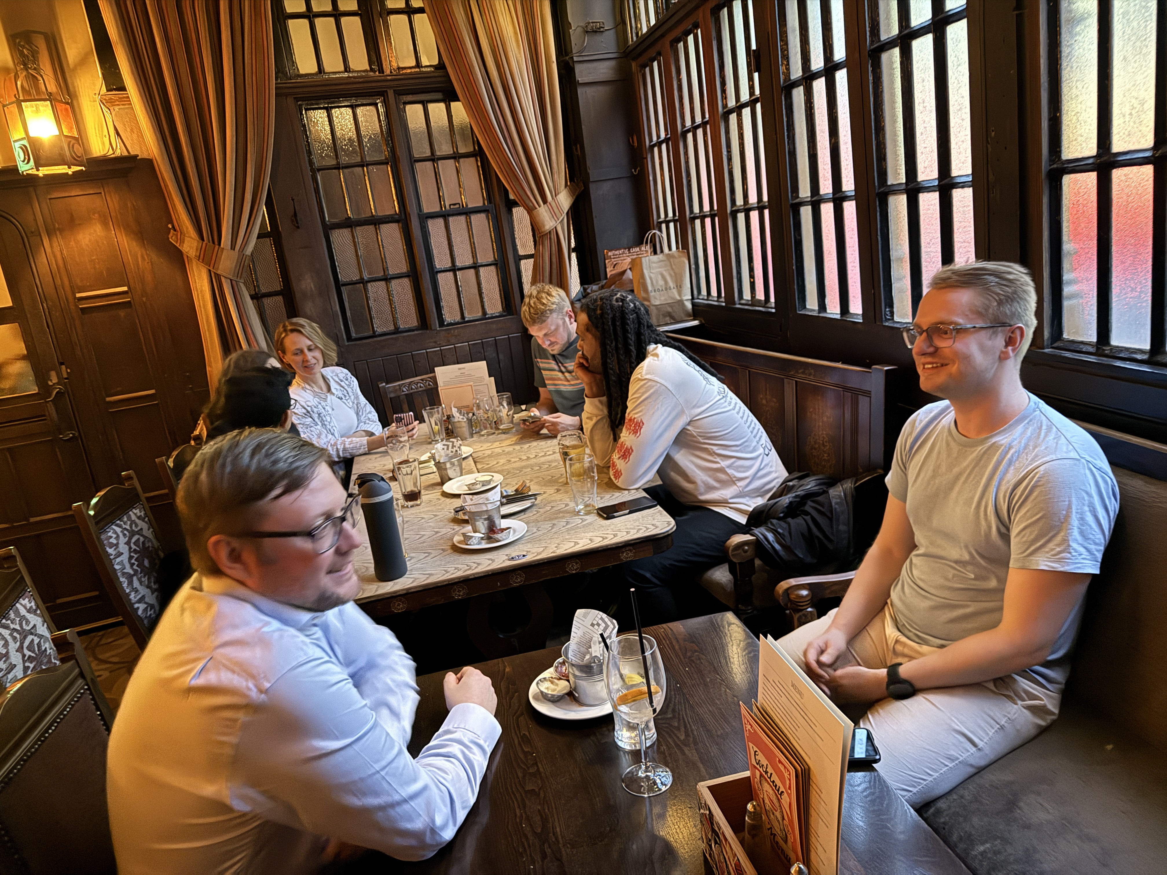 A small group of people sat in a wood panelled London pub.  image