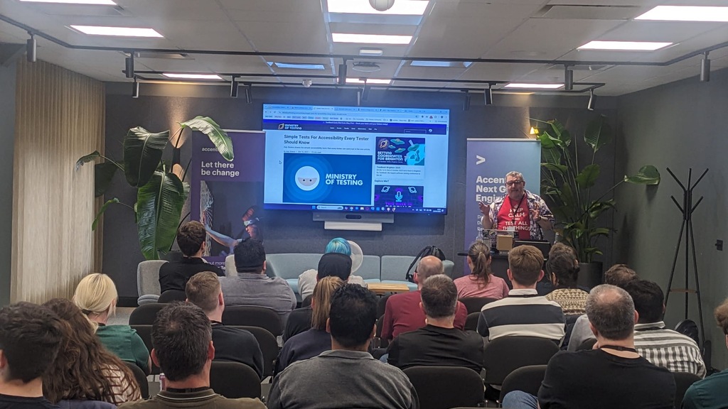 Ady Stokes presenting accessibility tests to an engaged MoT Leeds audience. Ady is wearing a red T-shirt and Hawaiian shirt with an accessibility is fundamental logo. 