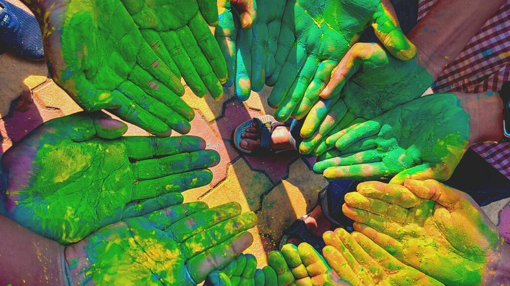 A circle of people extending their hands out, palms up, hands rubbed down with green chalk, signifying unity and cele... image