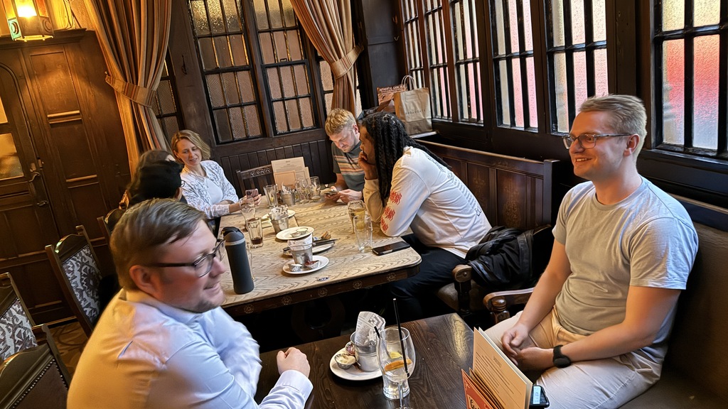 A small group of people sat in a wood panelled London pub.  image