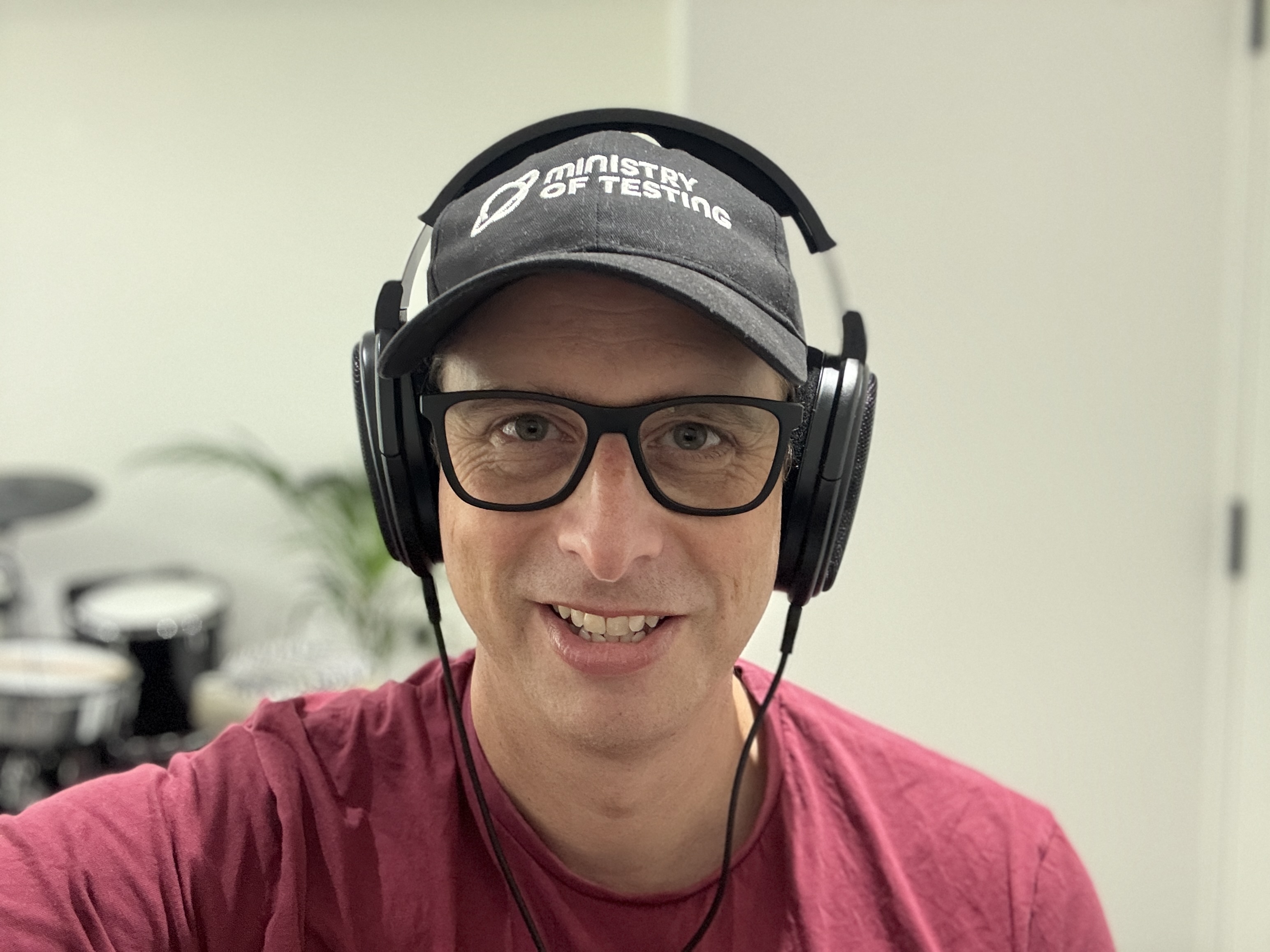 A selfie of a middle-aged white man with glasses. He is wearing headphones and a Ministry of Testing cap. 