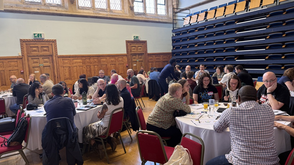 A group of people in a workshop setting gathered around tables.  image