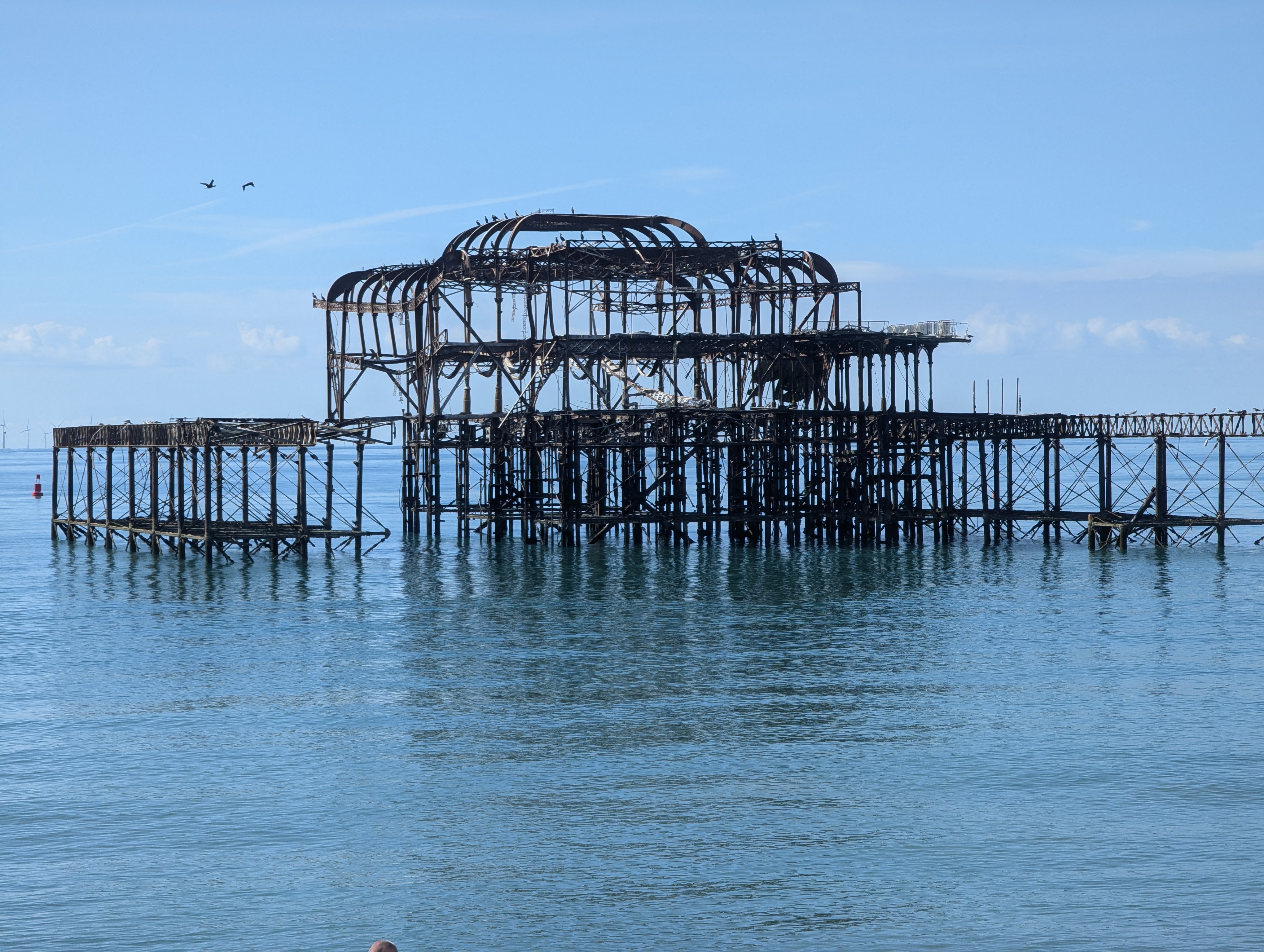 A photo of a burnt down West Pier in calm blue sea water.