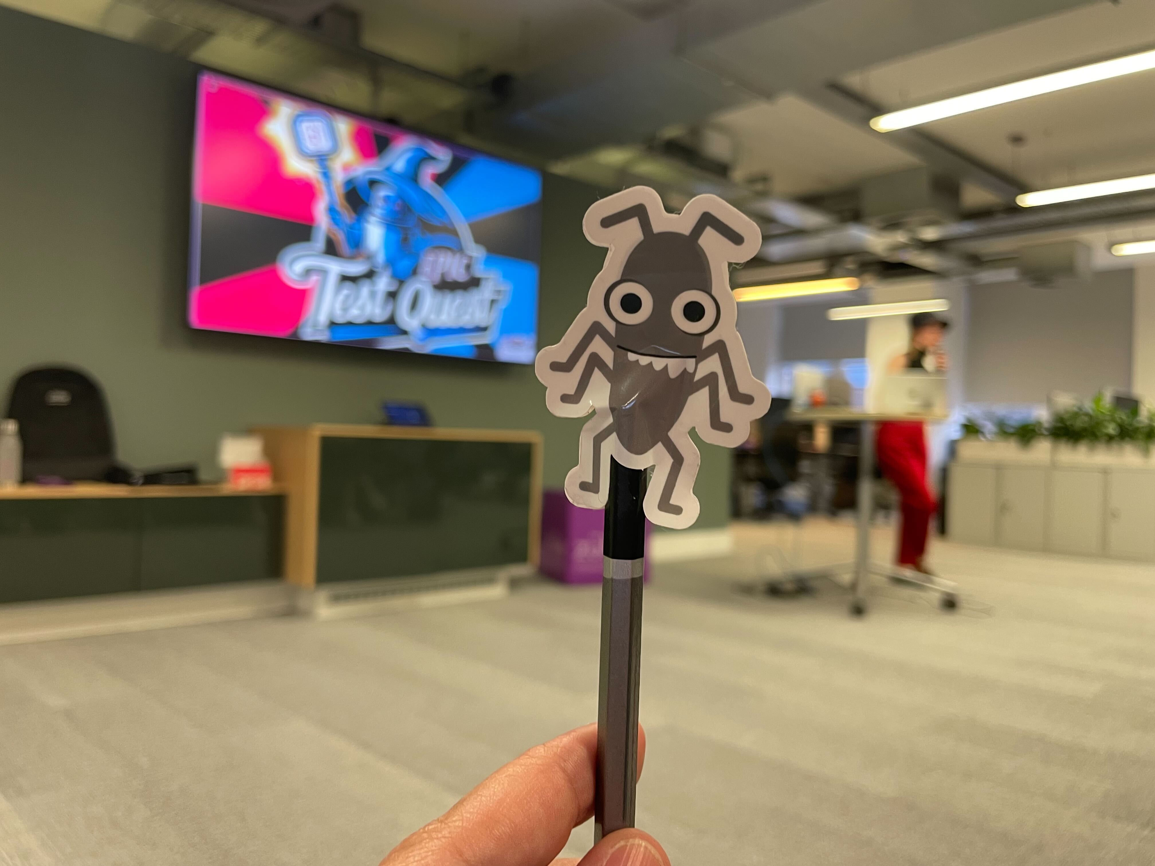 A photo of bug, a sticker, with Christine Pinto presenting her talk in the background.