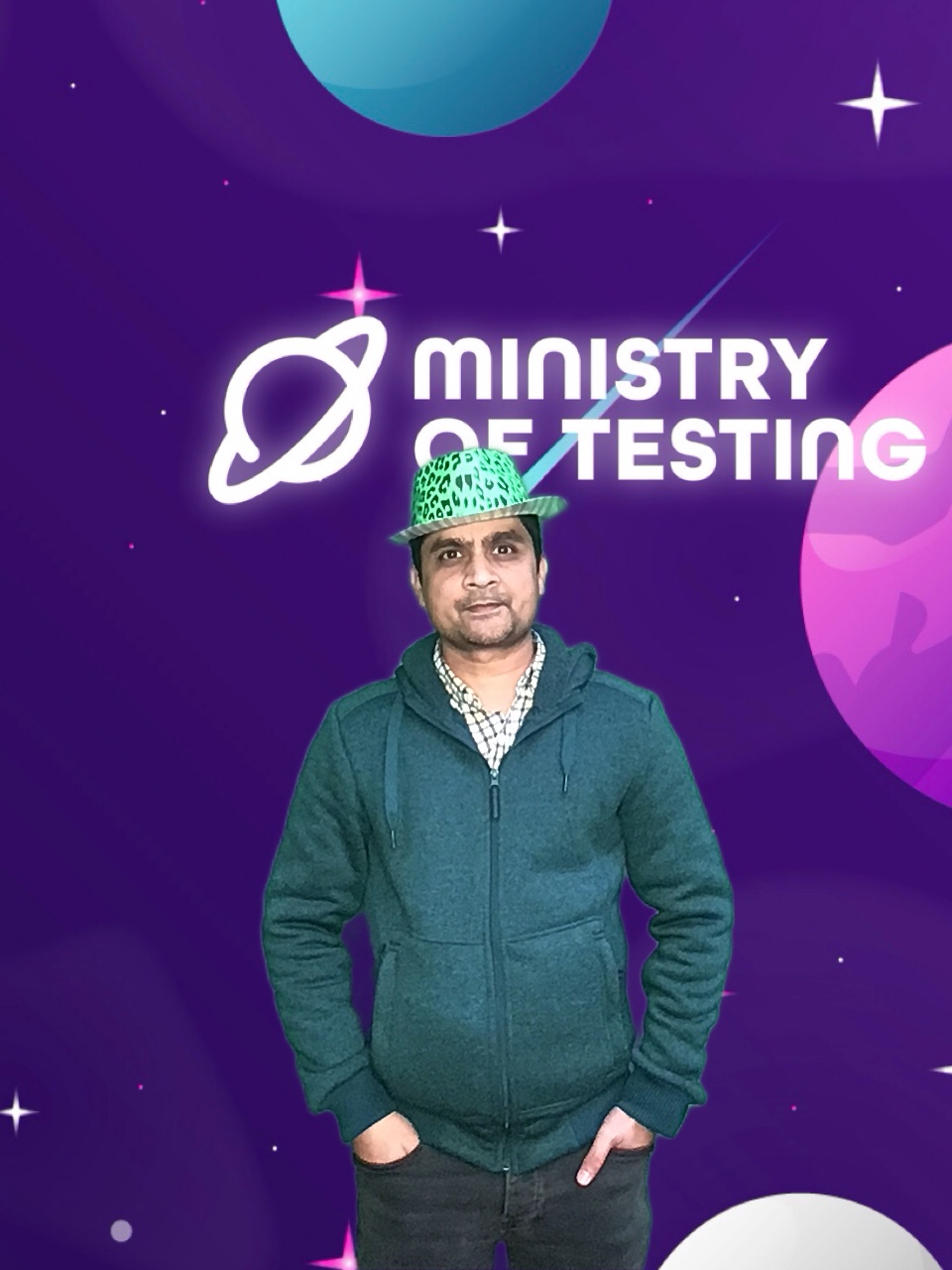 Here we have a solo photo booth entry from a TestBash 2024 attendee. They are wearing a green hoody with a checkered shirt underneath and have a silly green leopard print hat on their head. They have their hands in their pockets and are looking at the camera. 

Background: The green screen backdrop depicts a simple illustrated outer space scene. The main colour is purple, with cute stars and planets in shades of pink, blue, and white. About a third of the way down the screen, a logo appears. It reads "Ministry of Testing" in bold white text with a blue shooting star behind it. Next to the text, in the same bold white style, is a line drawing of the planet Saturn.