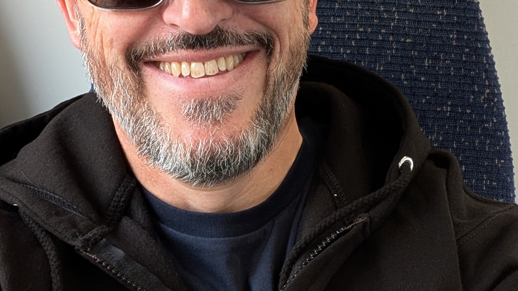 Smiling white male with a black and grey beard..Wearing a black and grey quality talks cap, a black quality talks hoo... image