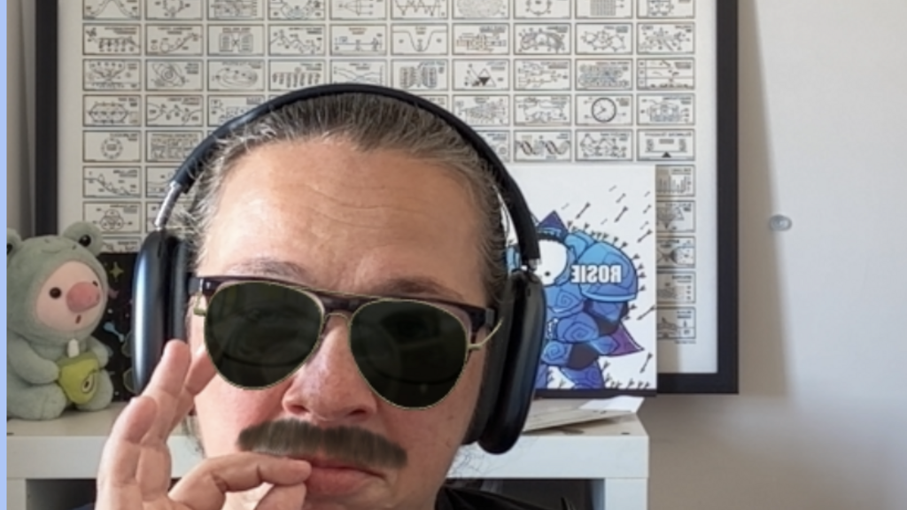 A Rosie screenshot from a virtual meeting, with sunglasses and a moustache. Her fingers are pinched, pretending she i... image