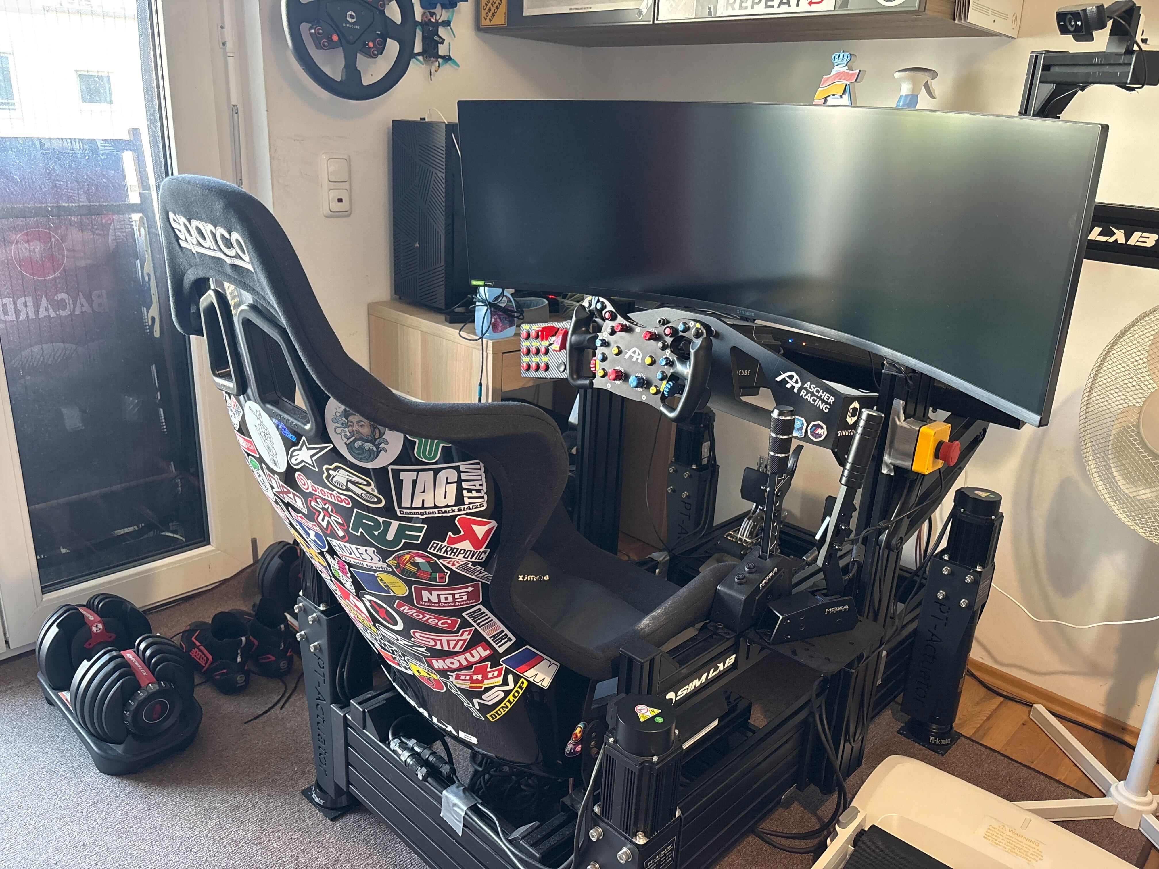 Picture of a sim racing rig with several stickers on the back of the seat.  Cosmo the Space Duck is there in real-life, hiding somewhere for you to find.