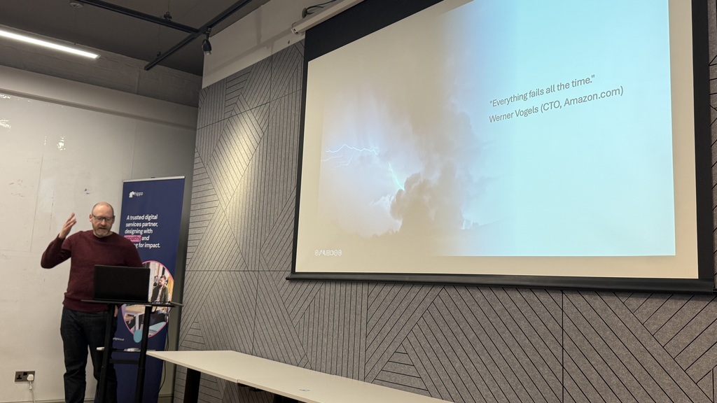 Alex, a male in black jeans and plum top who is wearing glasses and has short hair and beard. Stands at the front wit... image