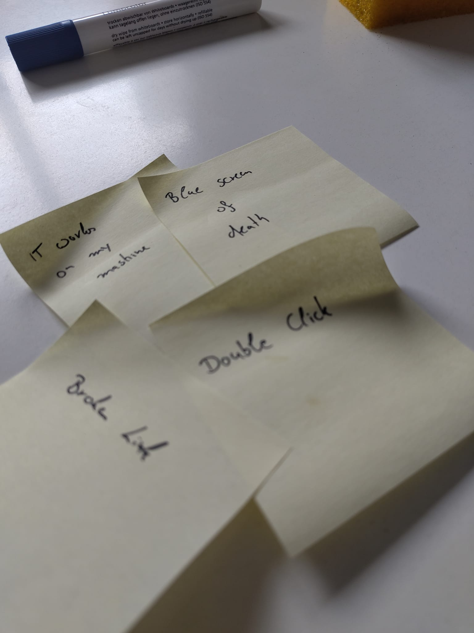 A blue whiteboard marker on a table next to 4 yellow post-its sticked to it reading "It works on my machine" (fun scenario), "bluescreen of death" (fun scenario), "broken link" (common issue) and "double click" (user action). Those were my points when I was on a roll and still convinced I would win this...