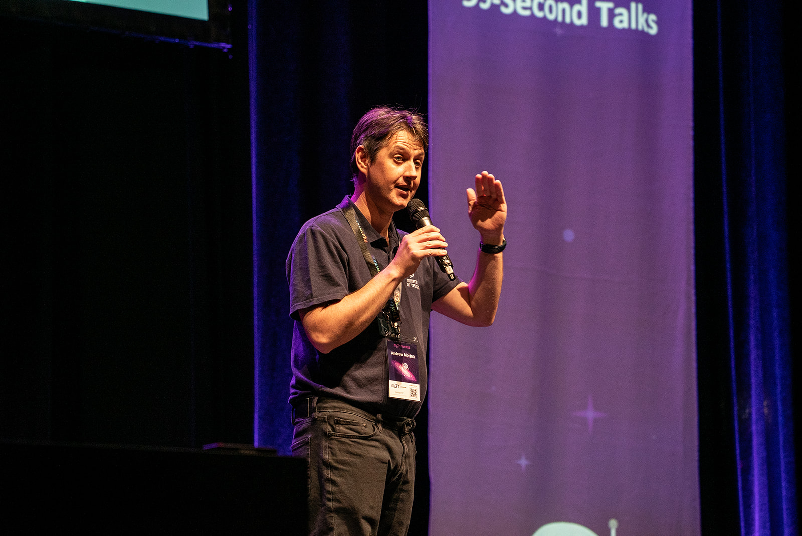 Andrew Morton on stage with his hand levelled at shoulder height to maybe show how tall Bug is, or maybe he's being funny with his puns.