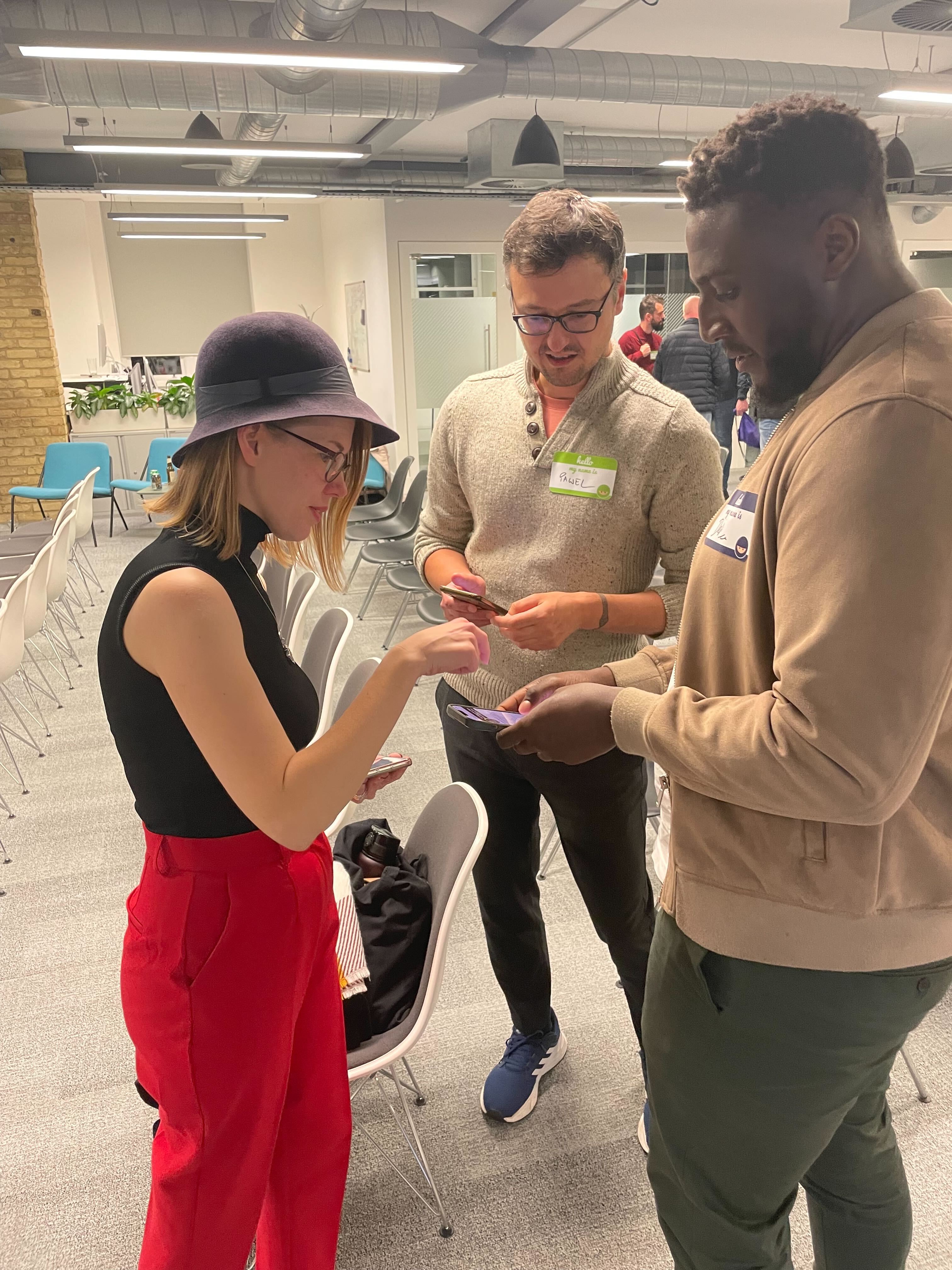 Christne, Deji and Pawel are chatting to one another. They have their phones out to connect with one another online.
