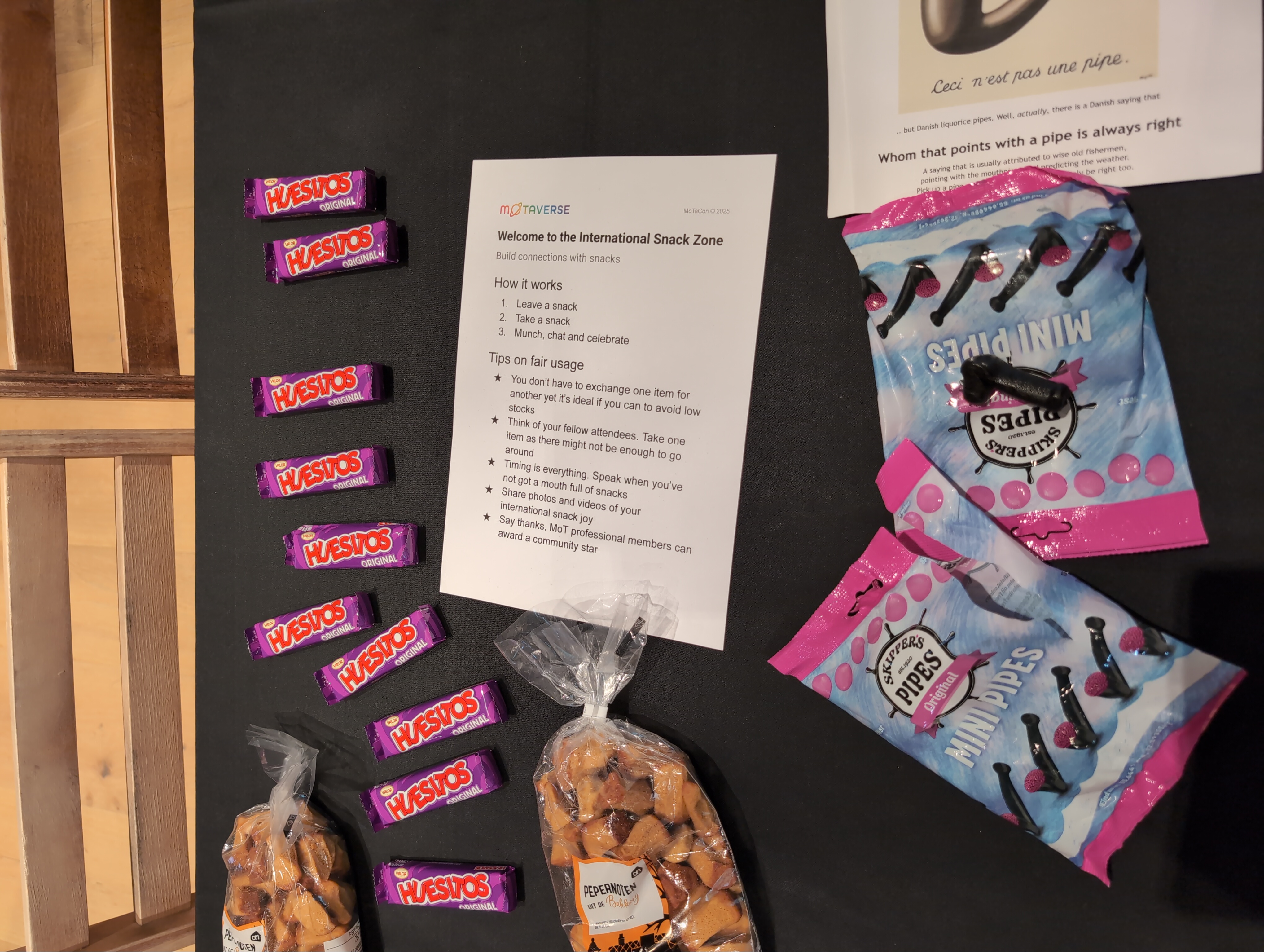 picture taken from above of a table with a few packaged snacks: chocolate bars, pepernoten, danish liquorice sweets, an A4 instruction sign