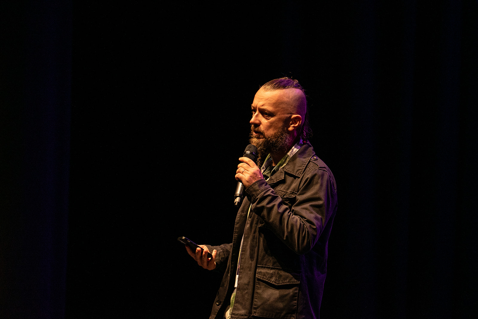 Jokin Aspiazu wearing a dark jacket, with a dark stage background, on the MoTaCon stage doing a 99 second talk.