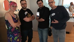 Four people. A woman and three men standing next to each other looking cool at the camera – they are attempting to look like they are in a band. One of them is holding a phone with a picture of ano... image