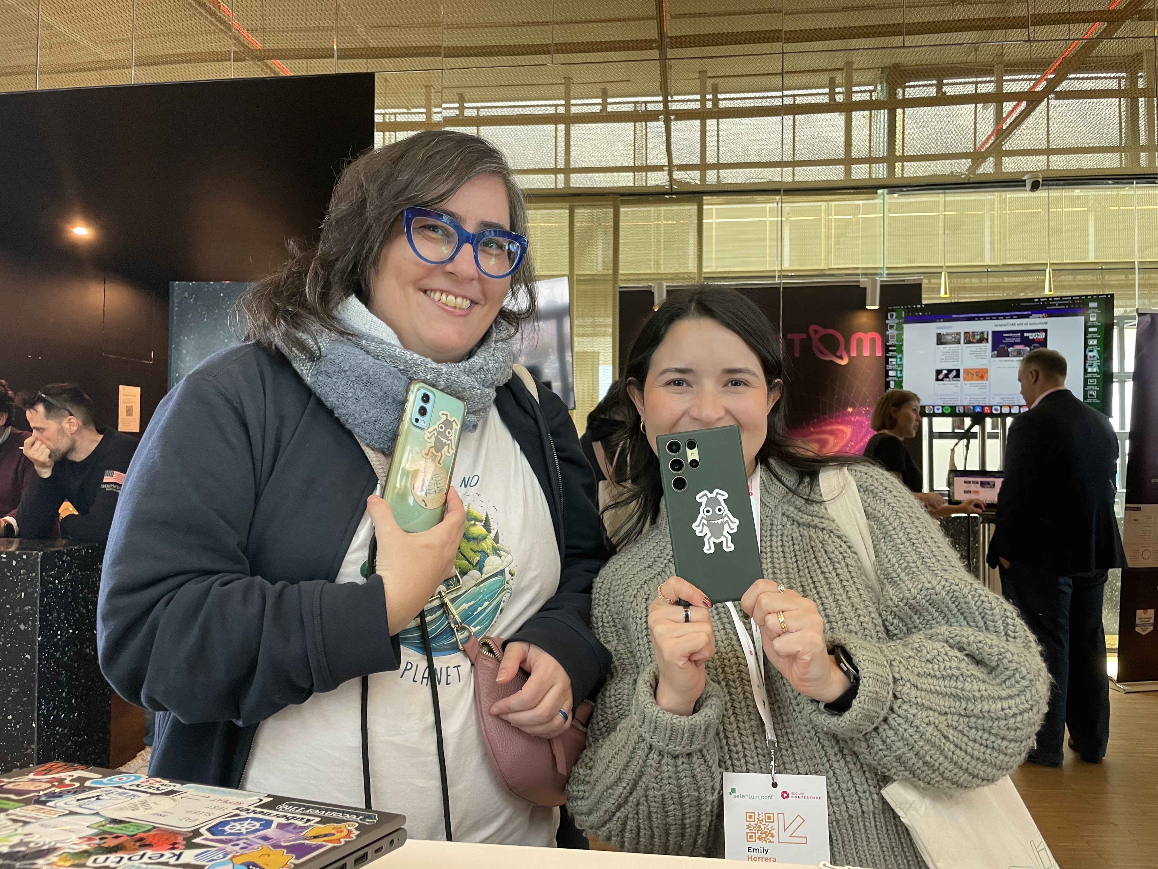 Two women posing for the camera and showing their phones with a 'bug' sticker on them.