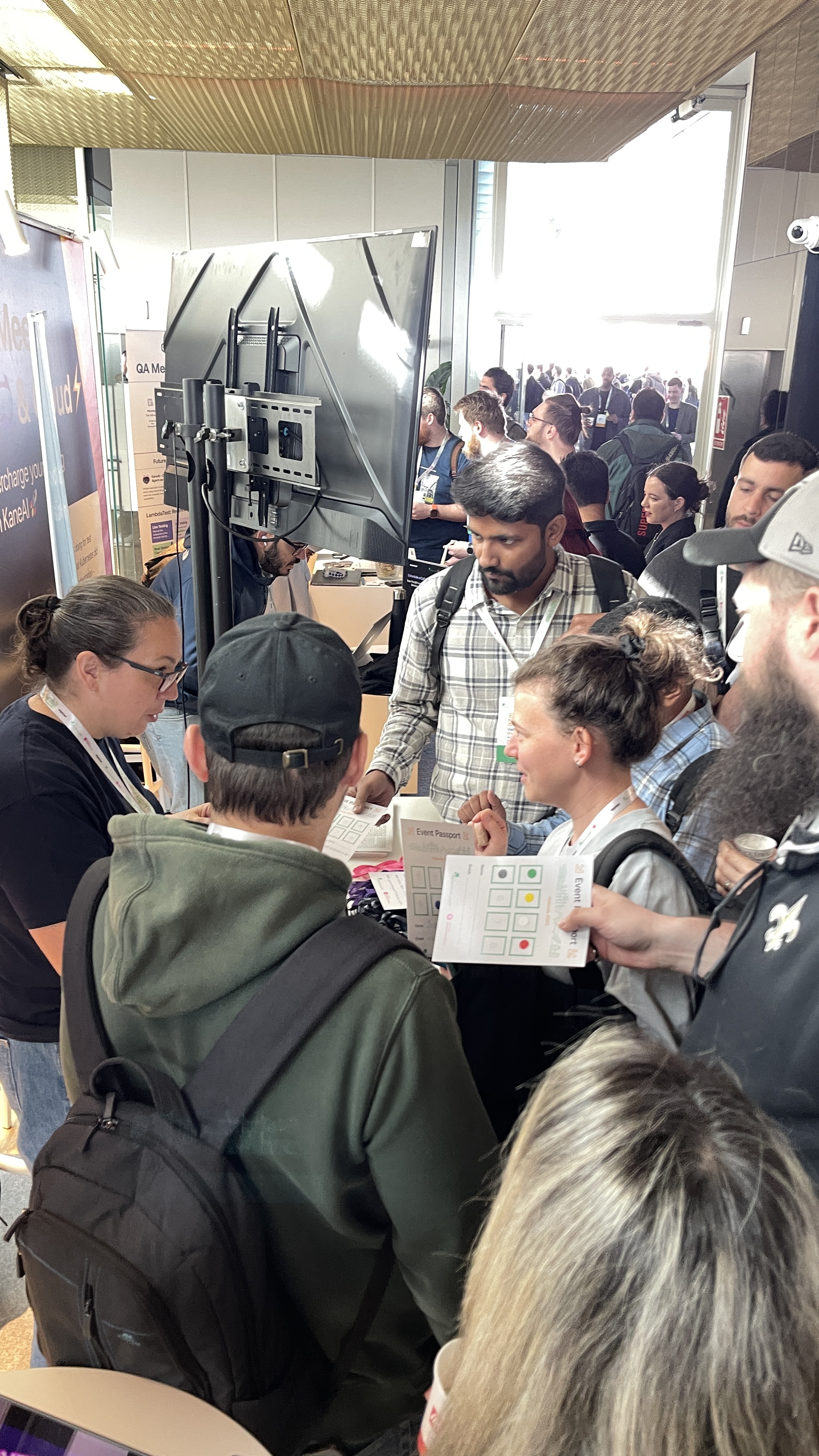 A large group of attendees crowds around the Ministry of Testing stand at Selenium Conf 2025, event passports in hand, as the sponsor raffle quiz kicks off. Rosie Sherry speaks to attendees while others engage with the challenge across the packed hallway.