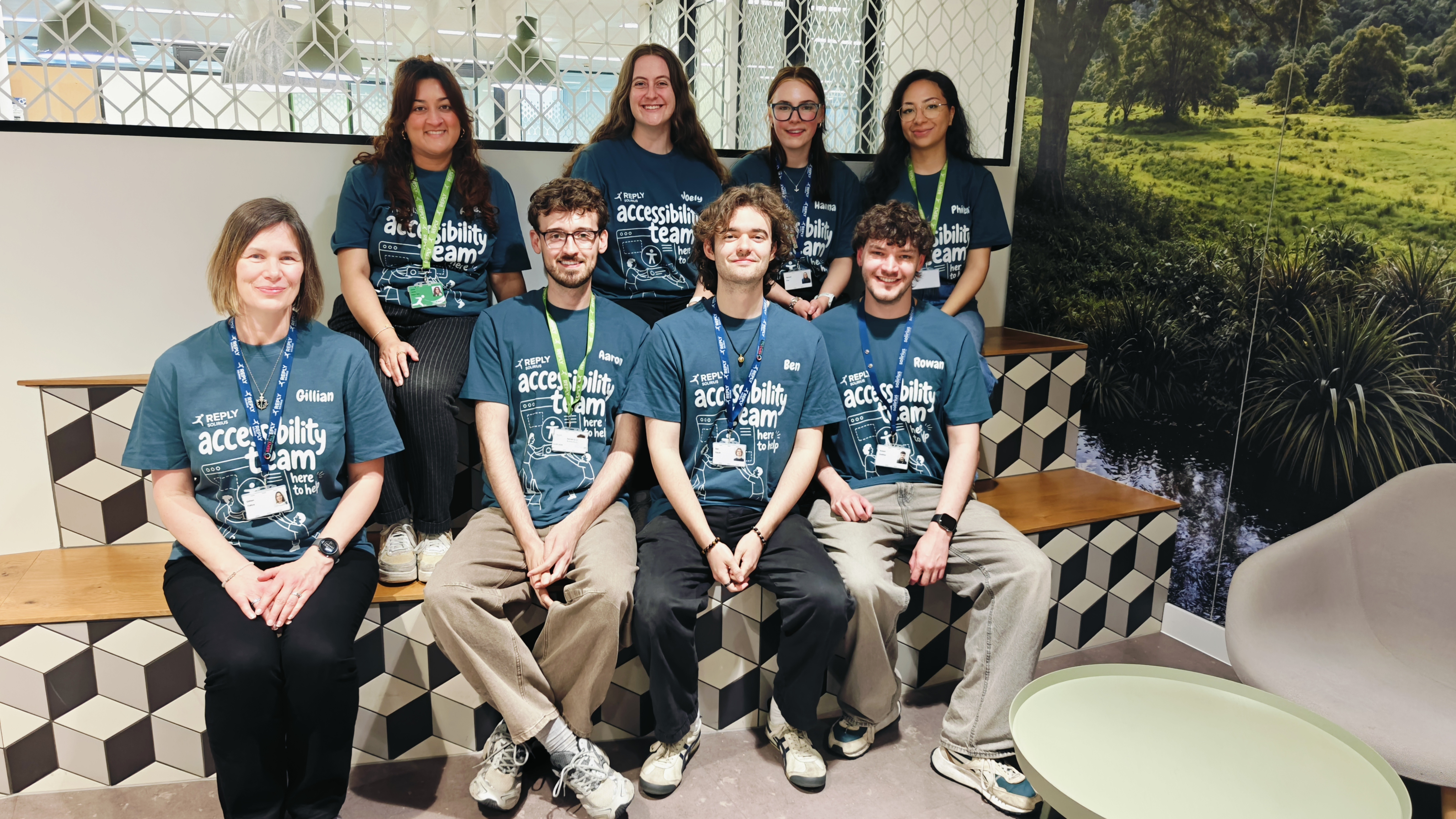 A smiling group photo of the accessibility team, taken on some tiered benches in the Reply office. The team are all w... image