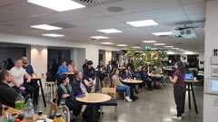A speaker facing an engaged and seated audience of 30 - 40 people in a room.  image