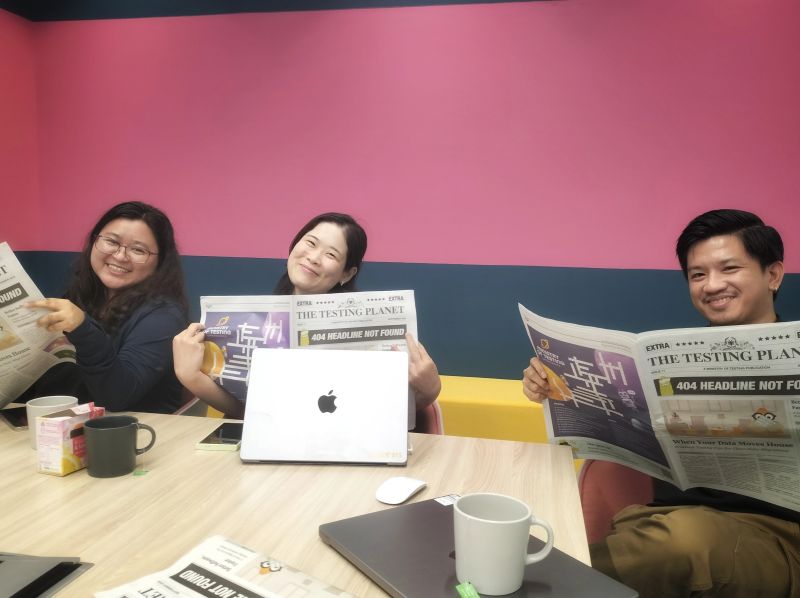 3 people sitting at a table posing whilst reading The Testing Planet newspaper.