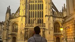 A Man wearing Ministry of testing bag pack, facing the Bath Abbey as the Sun sets over it. image