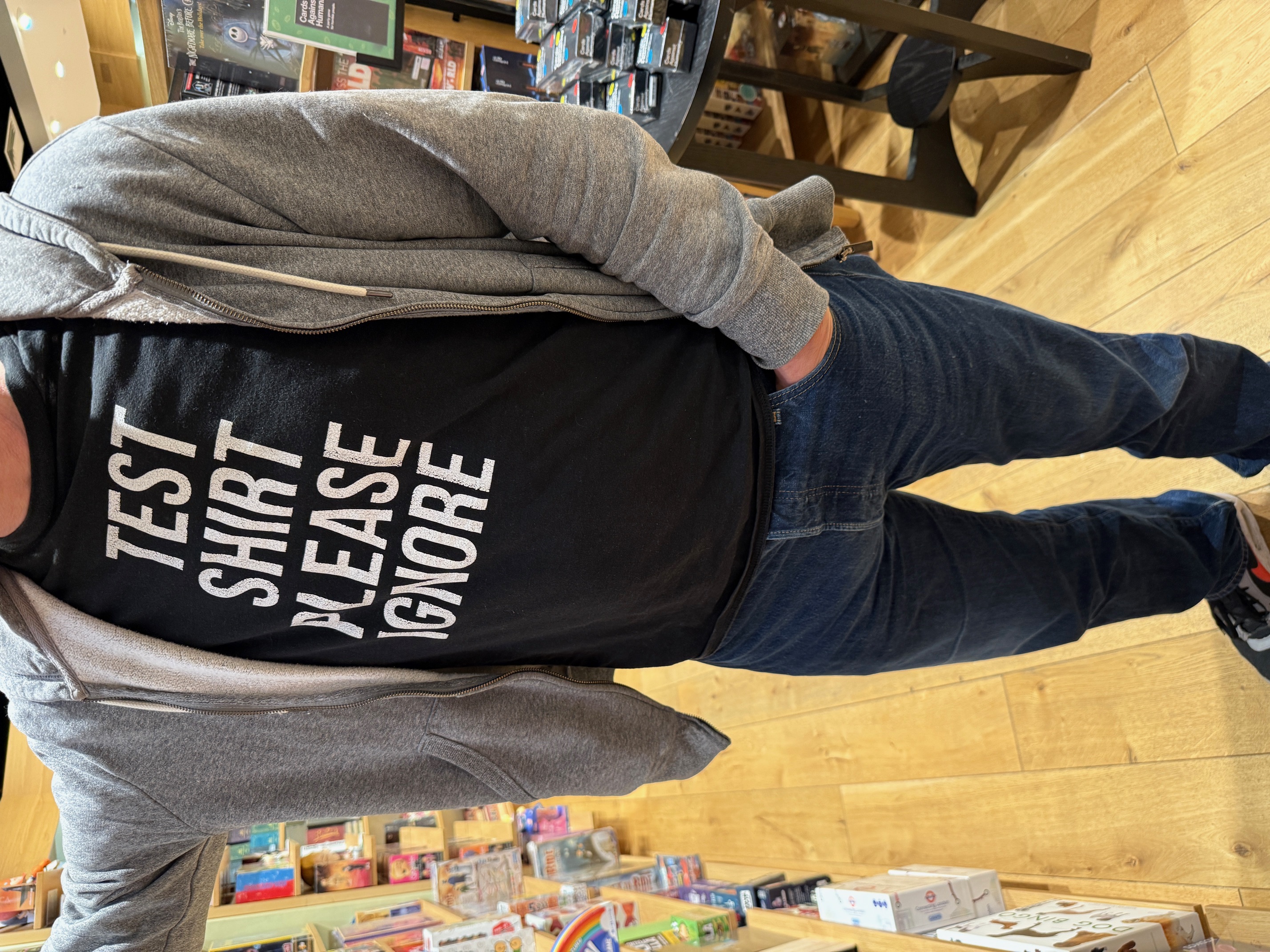 A man standing in a bookstore wearing a black t-shirt with white writing: test shirt please ignore. His face is not included in the original photo to protect his identity. 