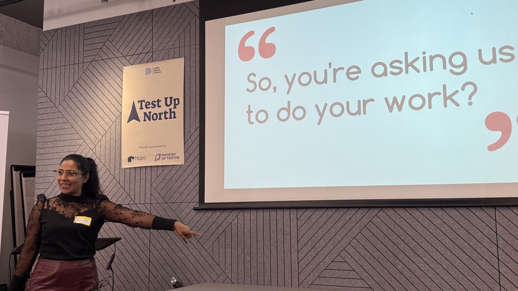 Suman presenting wearing a black top and red leather skirt. The screen shows the quote, ‘So, you’re asking us to do your work?’