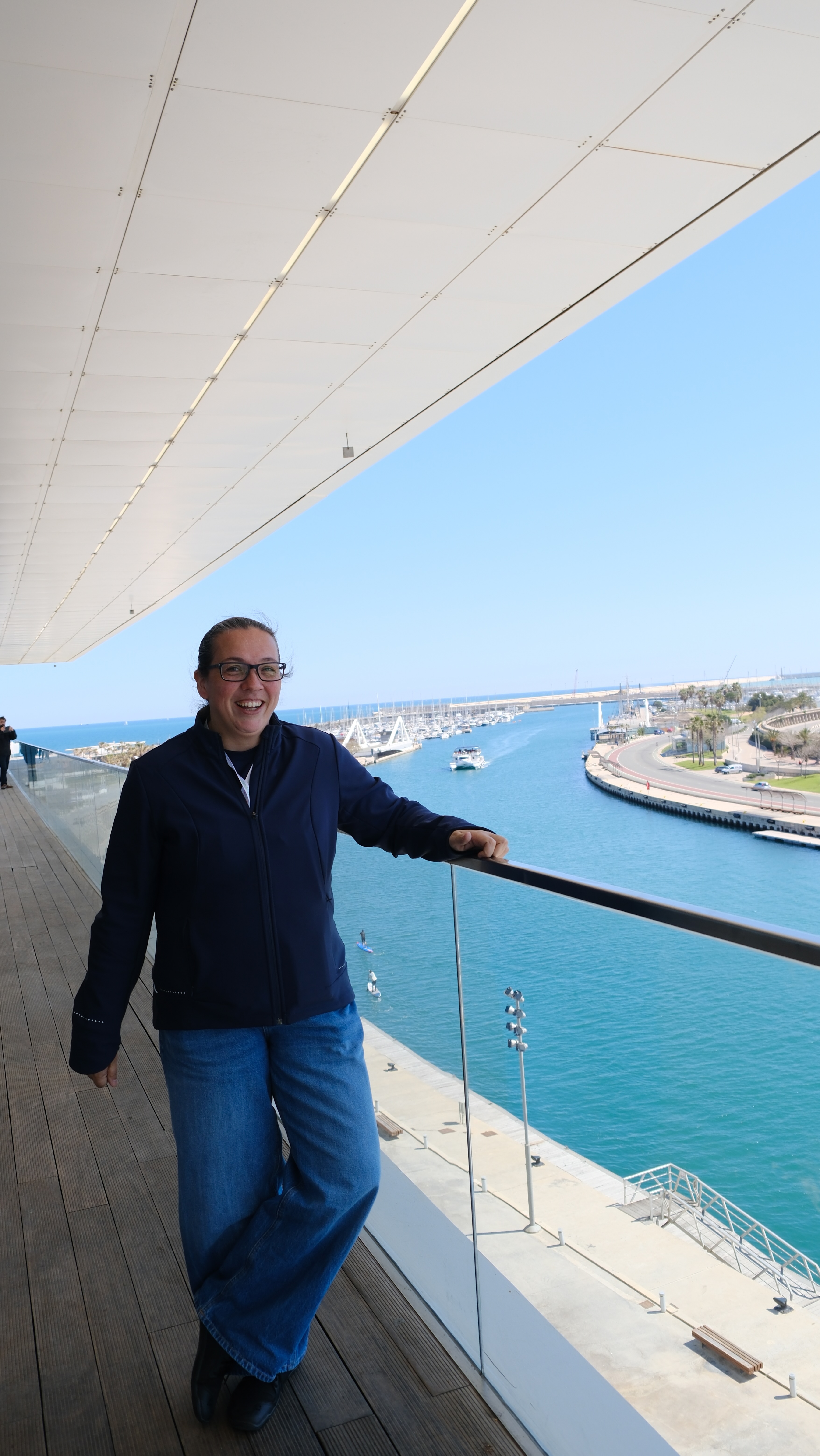 Rosie Sherry, CEO and founder of Ministry of Testing, smiles while leaning on a glass railing with the sparkling Mediterranean Sea and Valencia’s marina behind her, captured during a quick break from the conference.