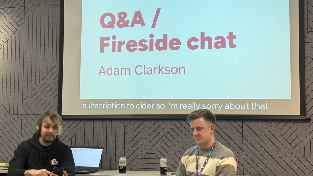 Adam and the host sit at the front with Q&amp;A / fireside chat on the screen behind them  image