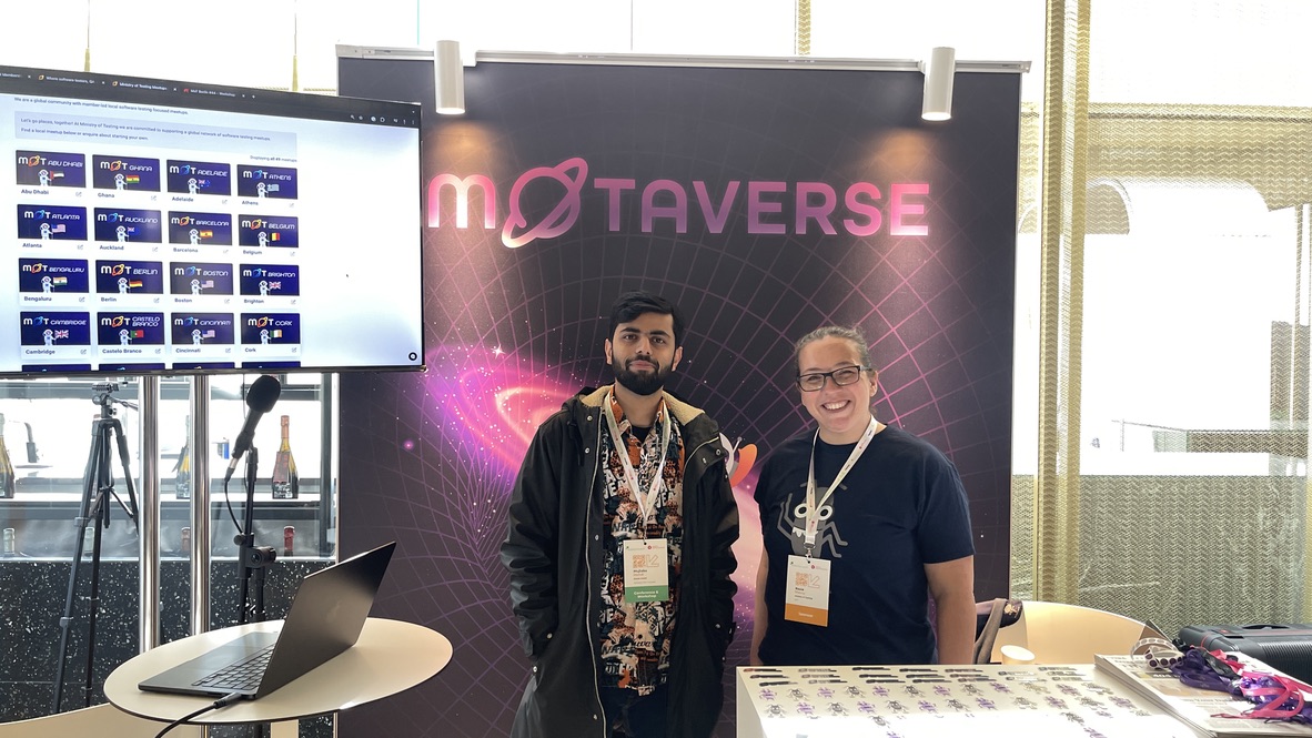 Mujtaba stands with Rosie Sherry at the Ministry of Testing stand at Selenium Conf 2025, smiling in front of the MoTaverse backdrop. A screen nearby displays MoT city meetup cards from around the world.