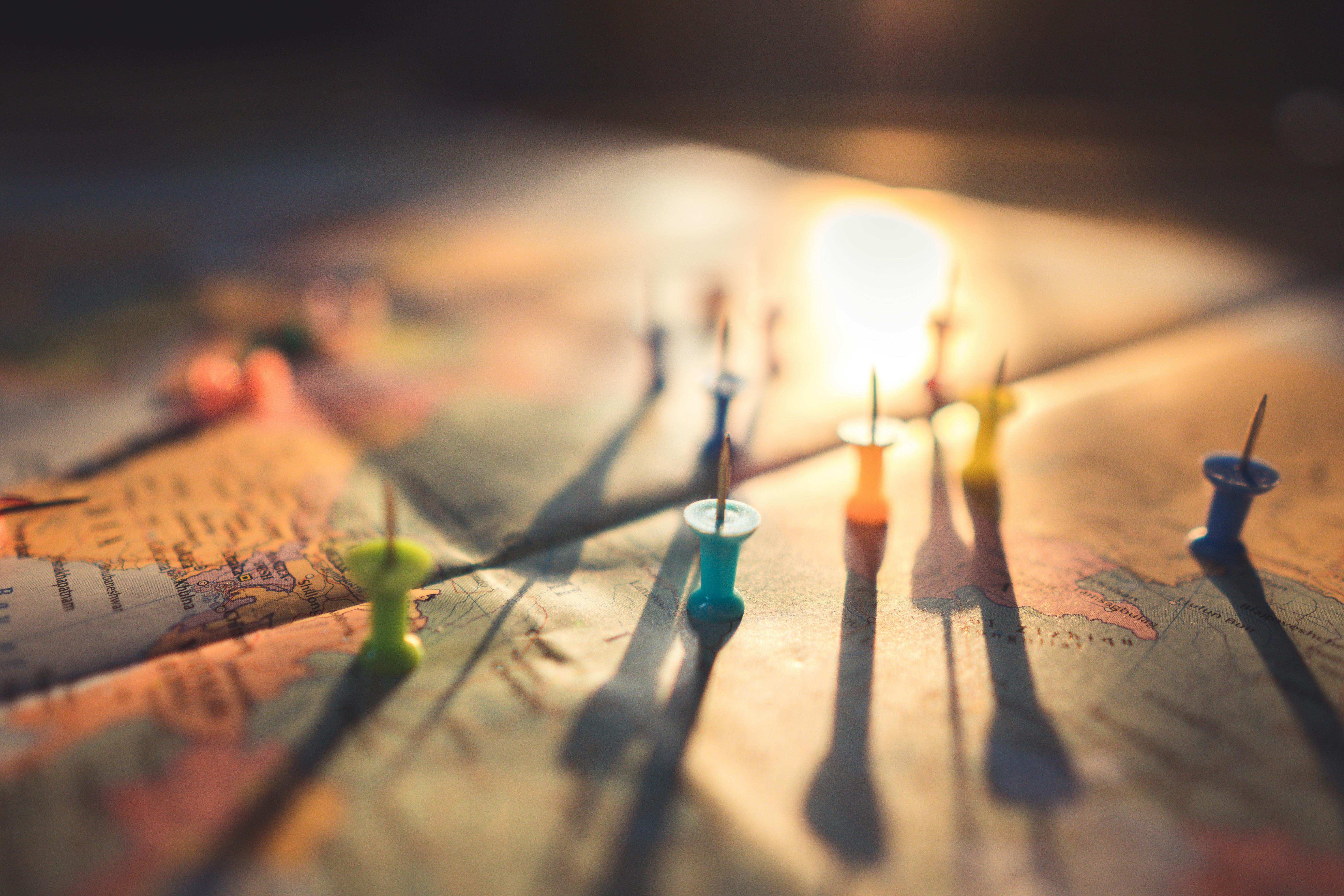 Close-up of a map with colorful push pins marking locations, lit by warm sunlight that casts long shadows across the ... image