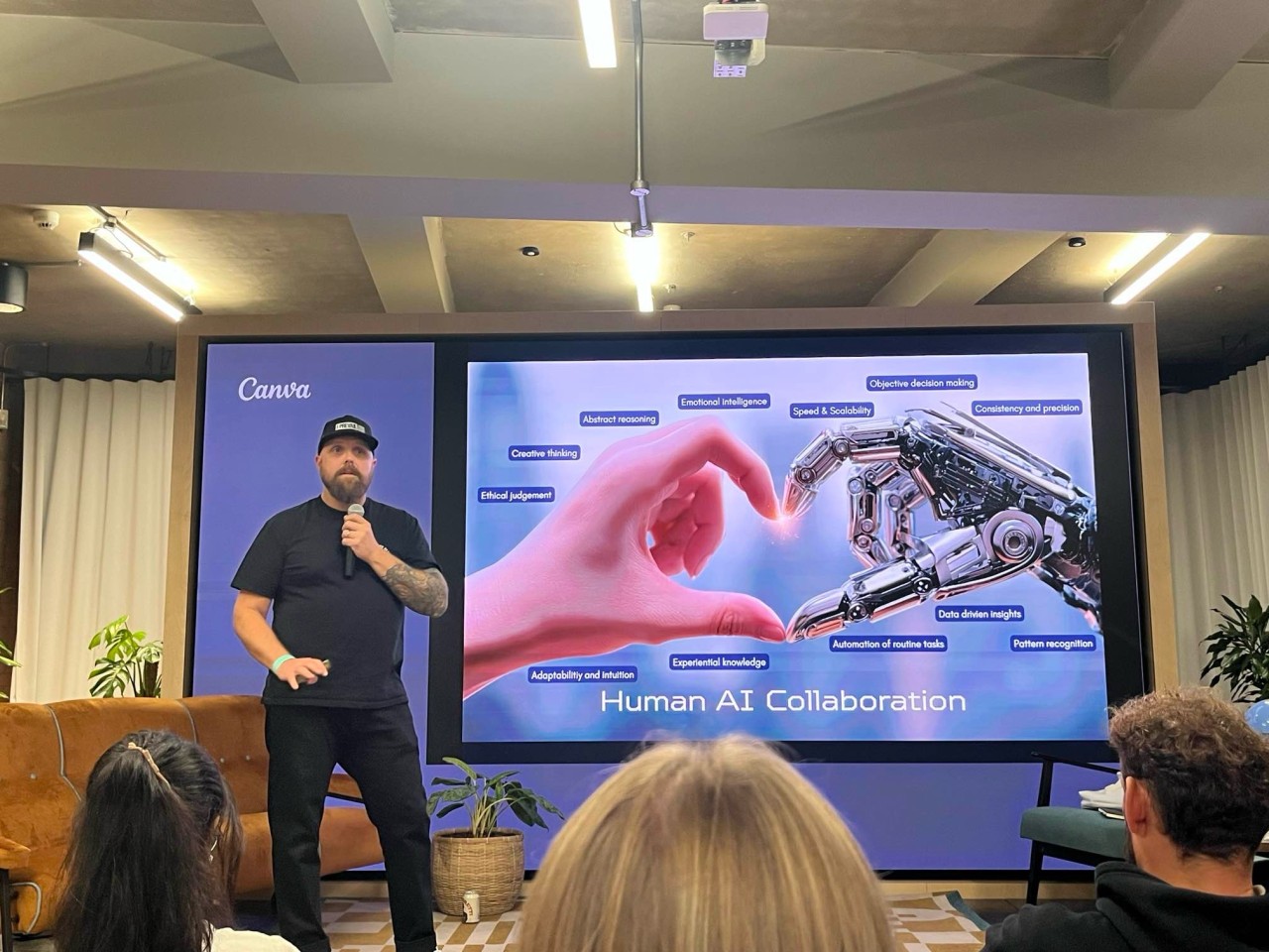 The photo shows Tom presenting his ideas on how established quality principles can be evolved to facilitate responsible AI development. Tom is standing on stage with a slide that shows a human hand and a robot hand making a heart. Around each hand are the key things that each brings: 
Humans with emotional intelligence, ethics, and critical thinking. 
AI with efficiency, speed, and automation.