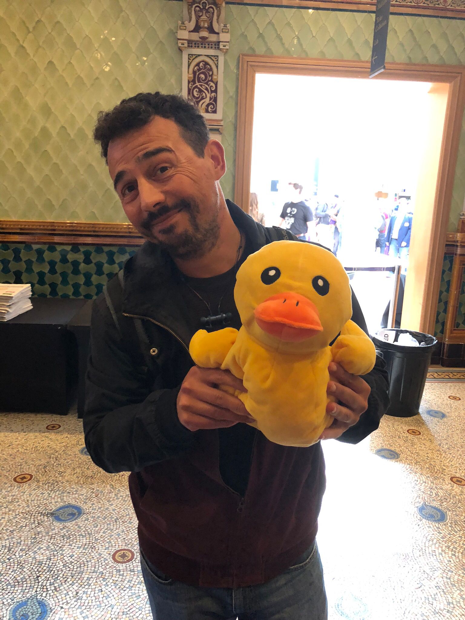 A male TestBash attendee wearing a dark jacket and jeans is holding a mid range yellow plush duck. Through his black beard he is showing a hint of smile.