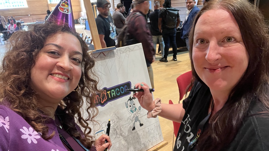 Donna and Ayesha posing with sharpies next to canvases of bug they are colouring in. image